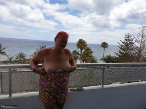 Obese nan with spiky red hair unveils her tits on balcony before posing naked